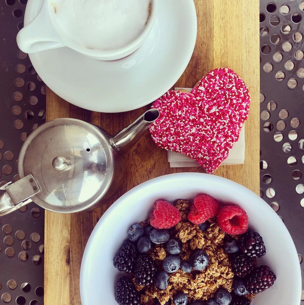 Mixed berries and granola with cappuccino and heart-shaped shortbread cookie.